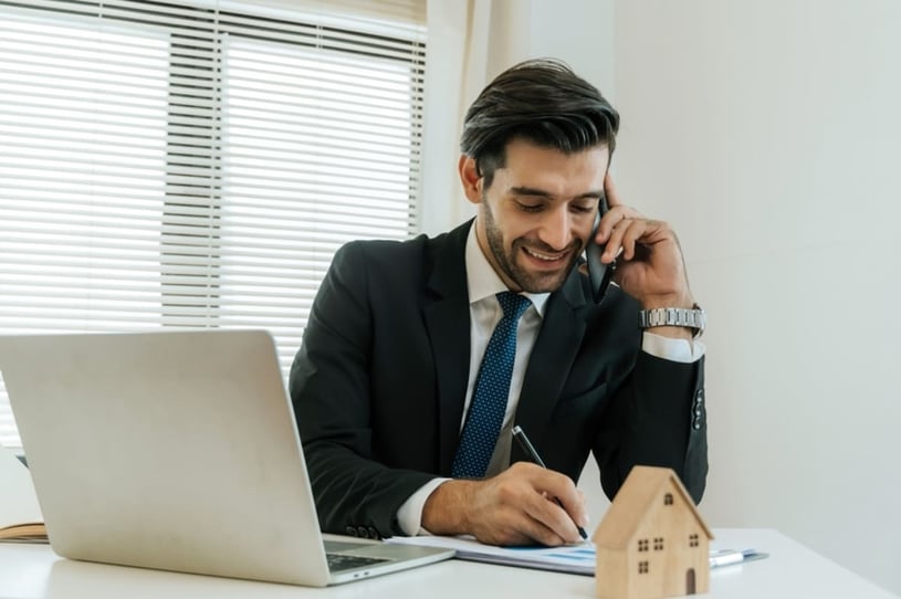 A businessman on the phone next to a laptop and a model home