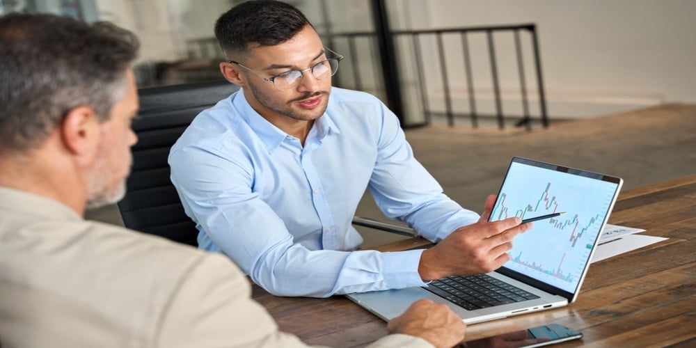 People in a meeting and pointing at a graph on a laptop