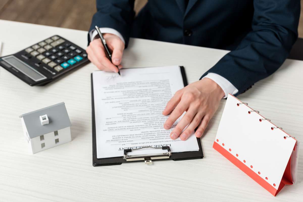 Cropped view of realtor signing lease agreement near blank calendar, calculator and house model (R) (S)