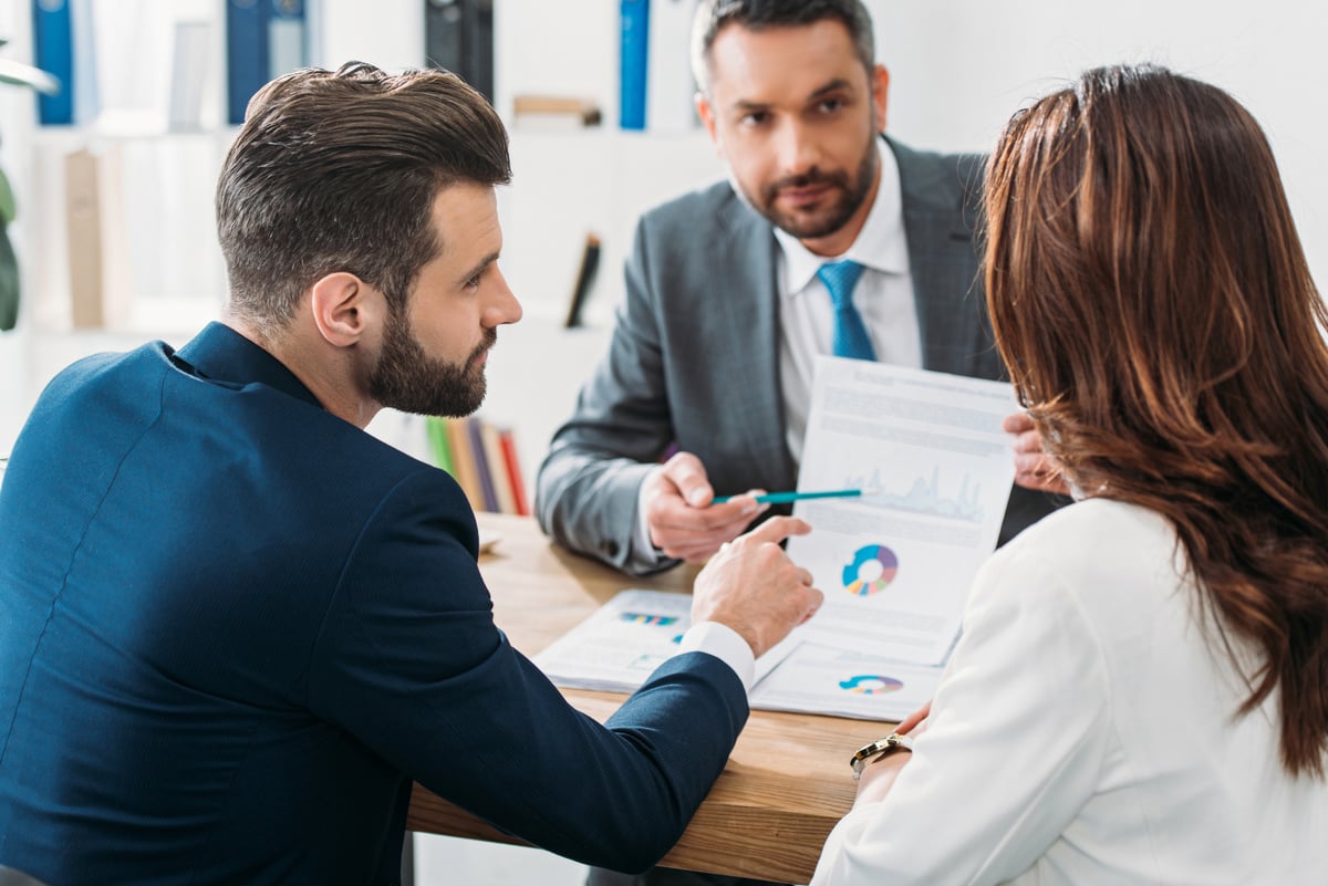 Selective focus of investor in suit pointing with finger at document at workspace